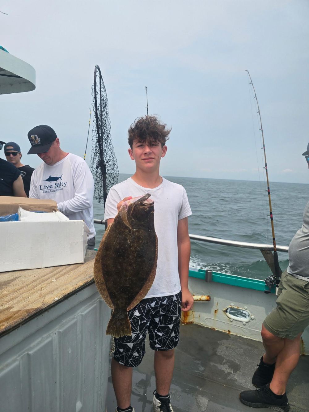 Boy holding a large fish on a boat with people in the background.