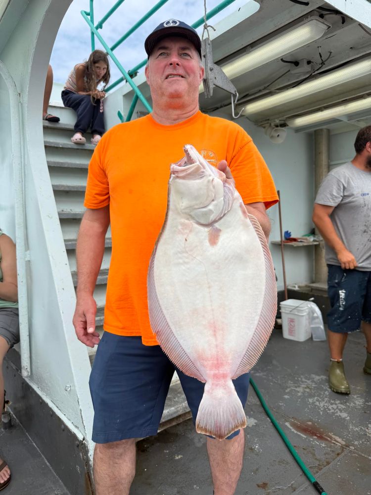 Man in orange shirt holding a large fish on a boat deck.