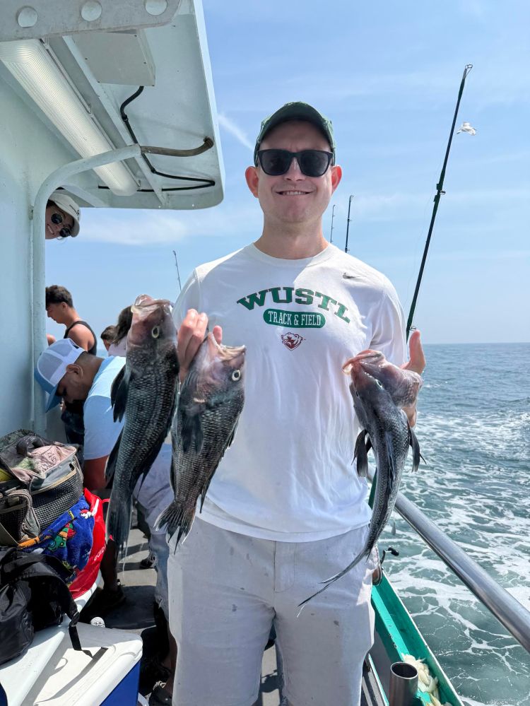 Person on a boat holding two fish, wearing sunglasses and a cap.