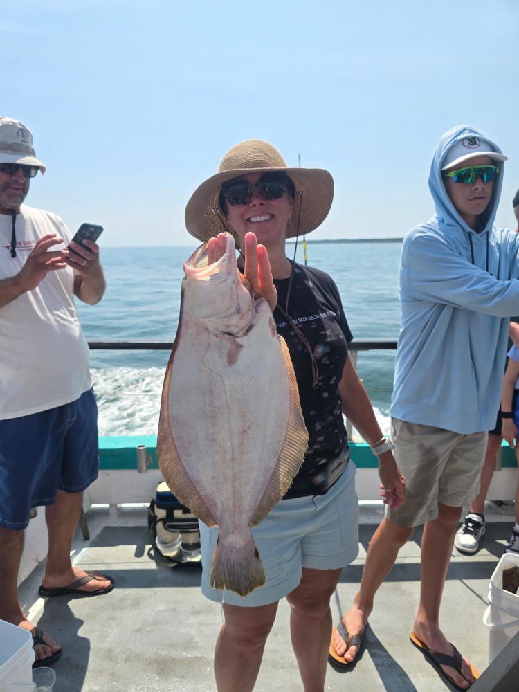 Person holding a large fish on a boat, surrounded by others taking photos.
