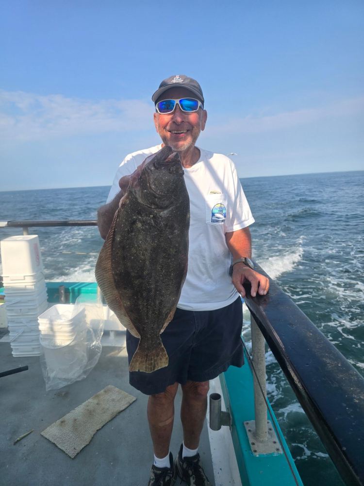 Person holding a large fish on a boat over the ocean.