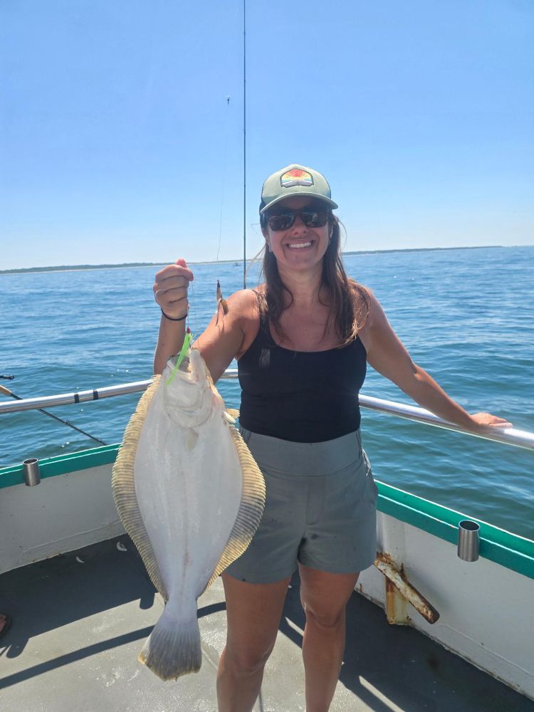 Smiling woman holding a large fish on a boat under a clear sky.