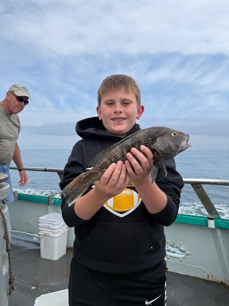 Boy on boat holding a fish, with an older man in the background.
