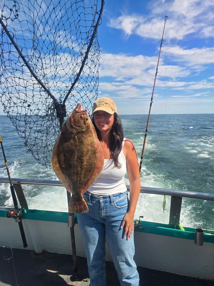 Person holding a large fish on a boat with ocean in the background.