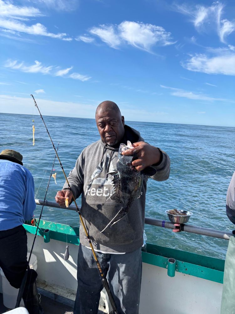 Man holding a fish on a boat under a clear blue sky.