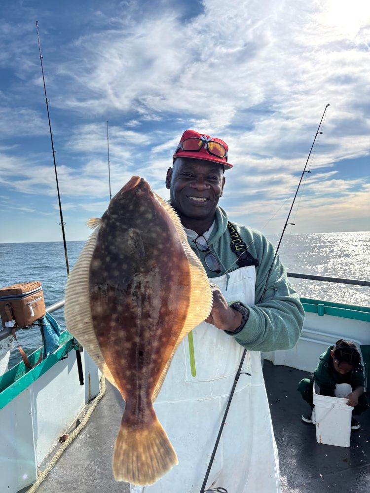 Person on a boat holding a large fish with two fishing rods visible against a cloudy sky.
