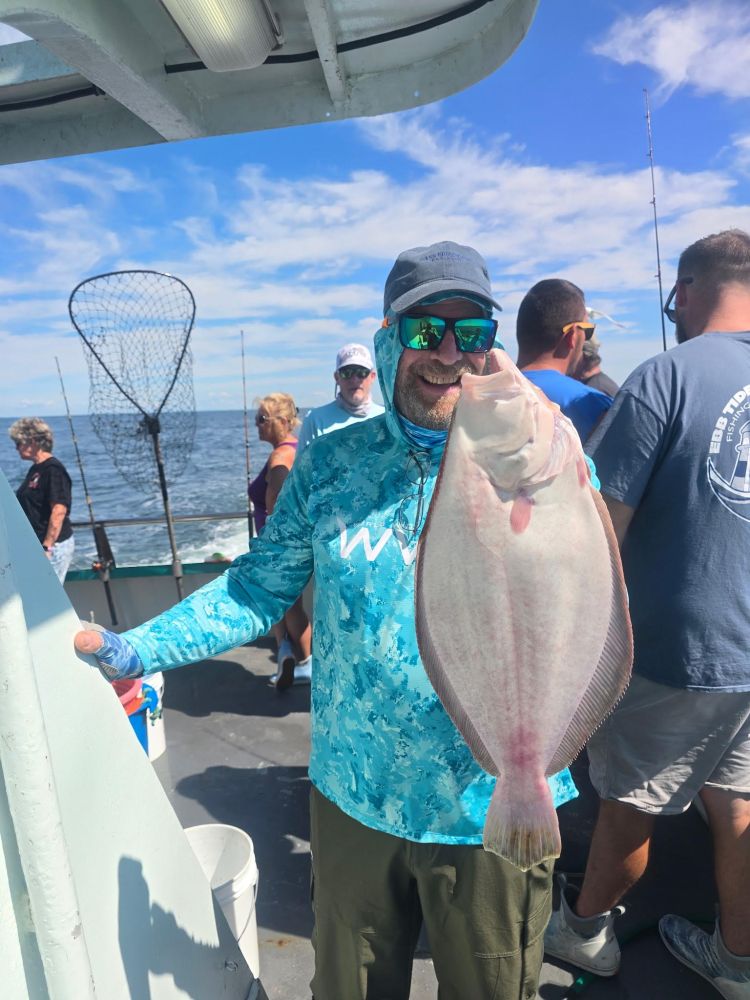 Man on a boat holding a large fish, with ocean in the background.