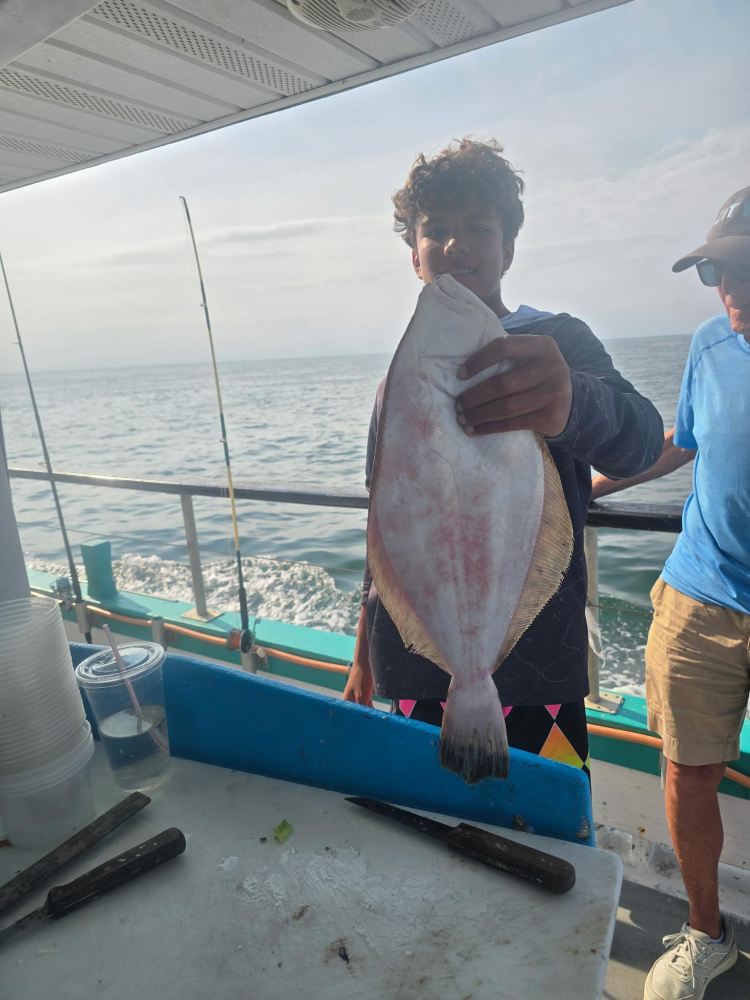 Person holding a large fish on a boat with ocean in the background.