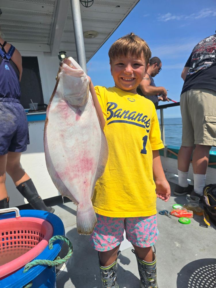 Child in yellow shirt holds large fish on a boat.