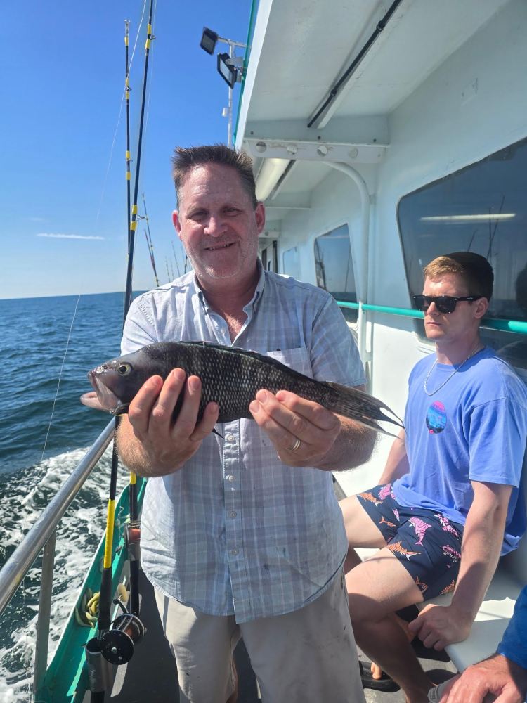 Man holding a fish on a boat with another man sitting.