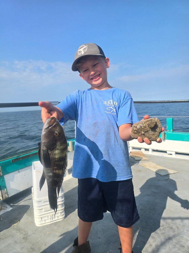 Boy on boat holding a fish and a rock, smiling.