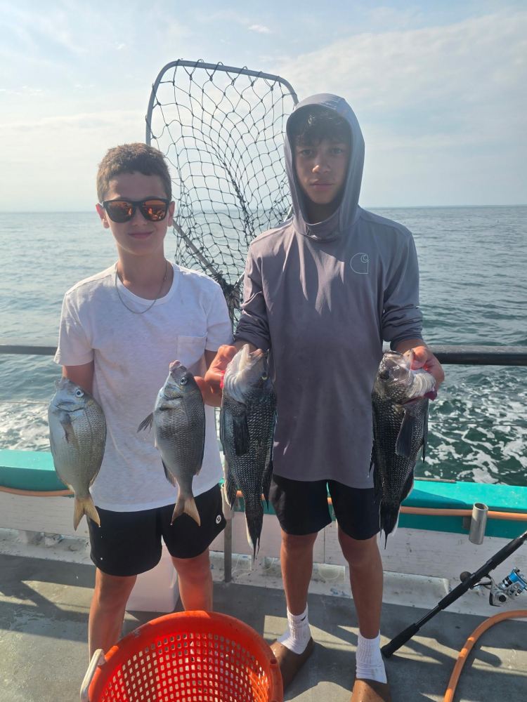 Two boys on a boat holding fish with a net in the background.
