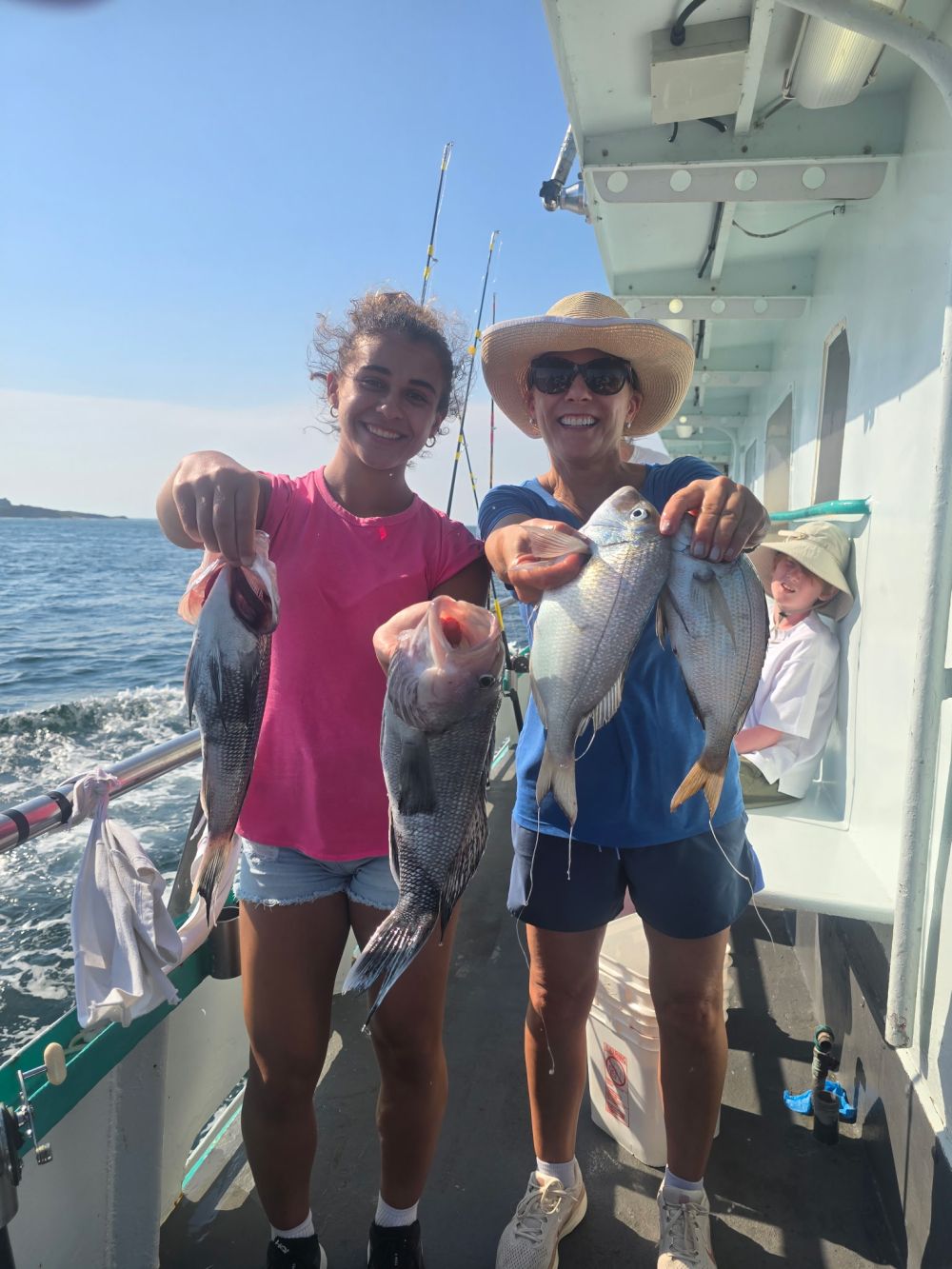 Two people smiling and holding fish on a boat with ocean background.