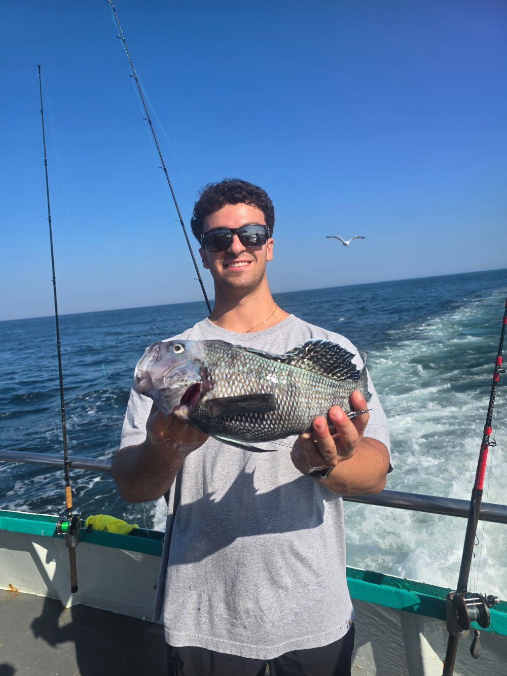 Man holding a fish on a boat with ocean and sky in the background.