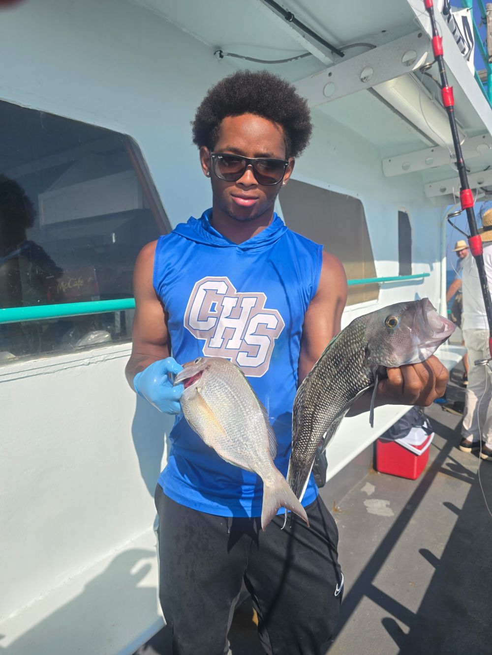 Person in blue shirt holding two fish on a boat.