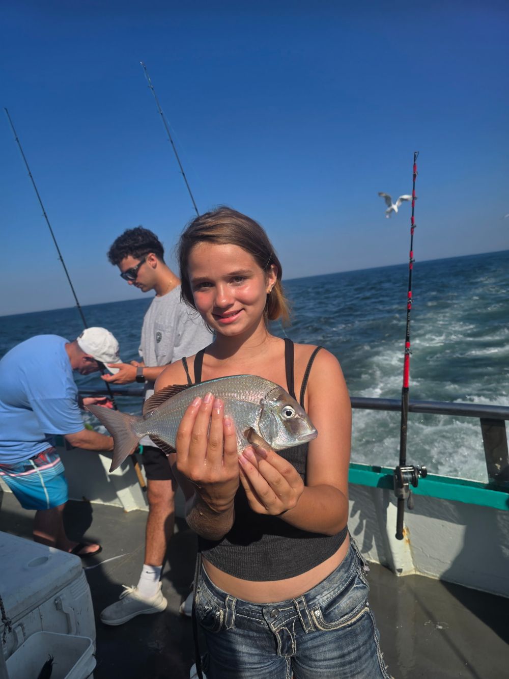 Person holding a fish on a boat with others and fishing rods.