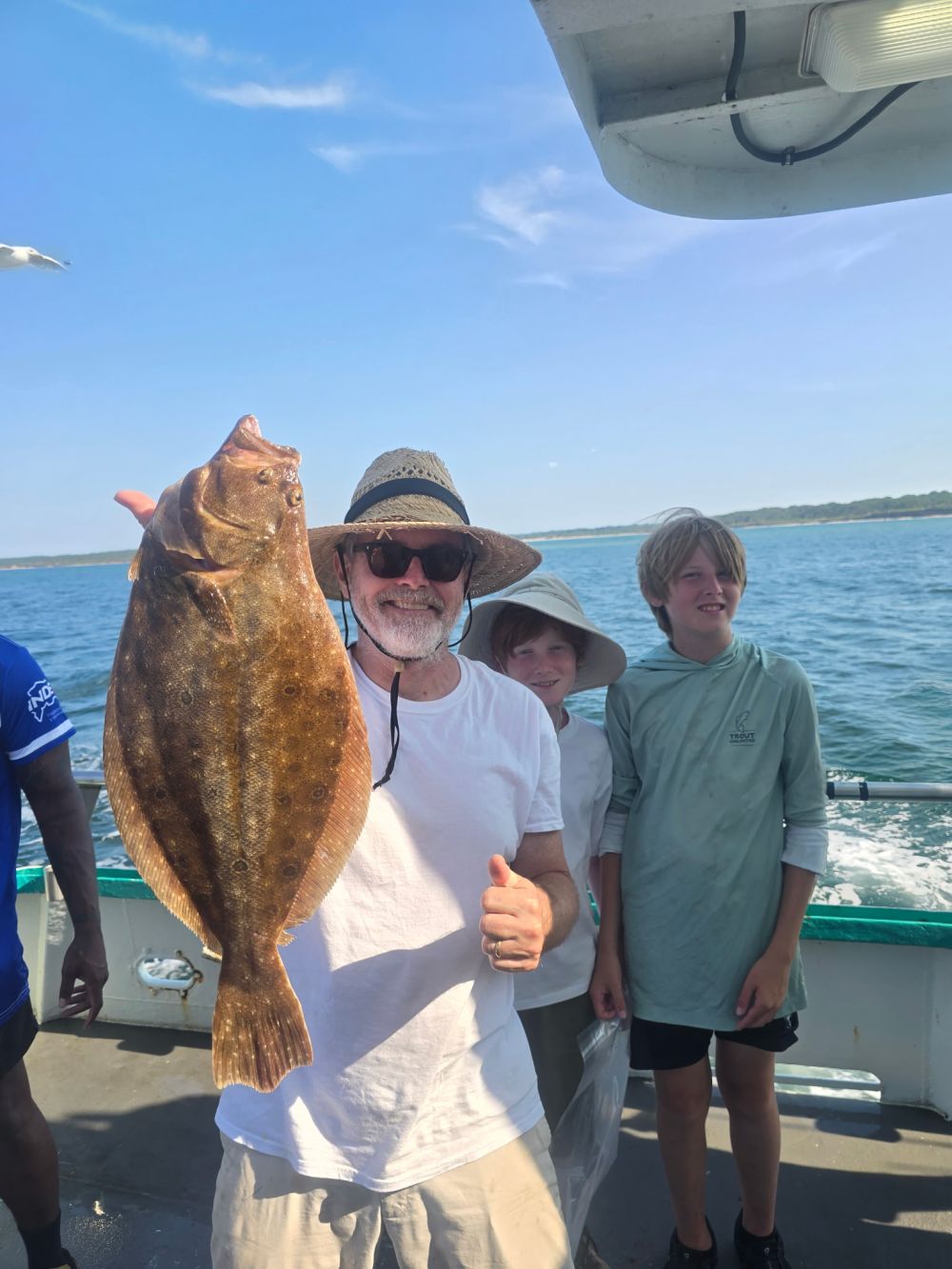 Man holding a fish on a boat with two boys, sunny day.
