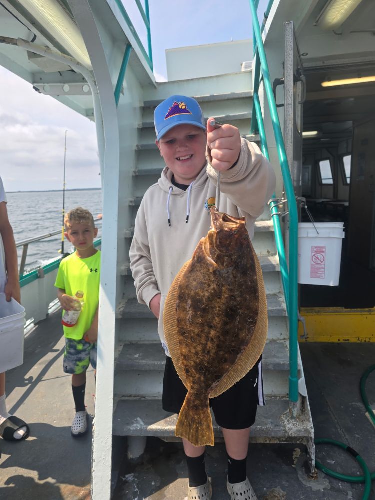 Boy holding a flatfish on a boat, smiling with a younger boy nearby.