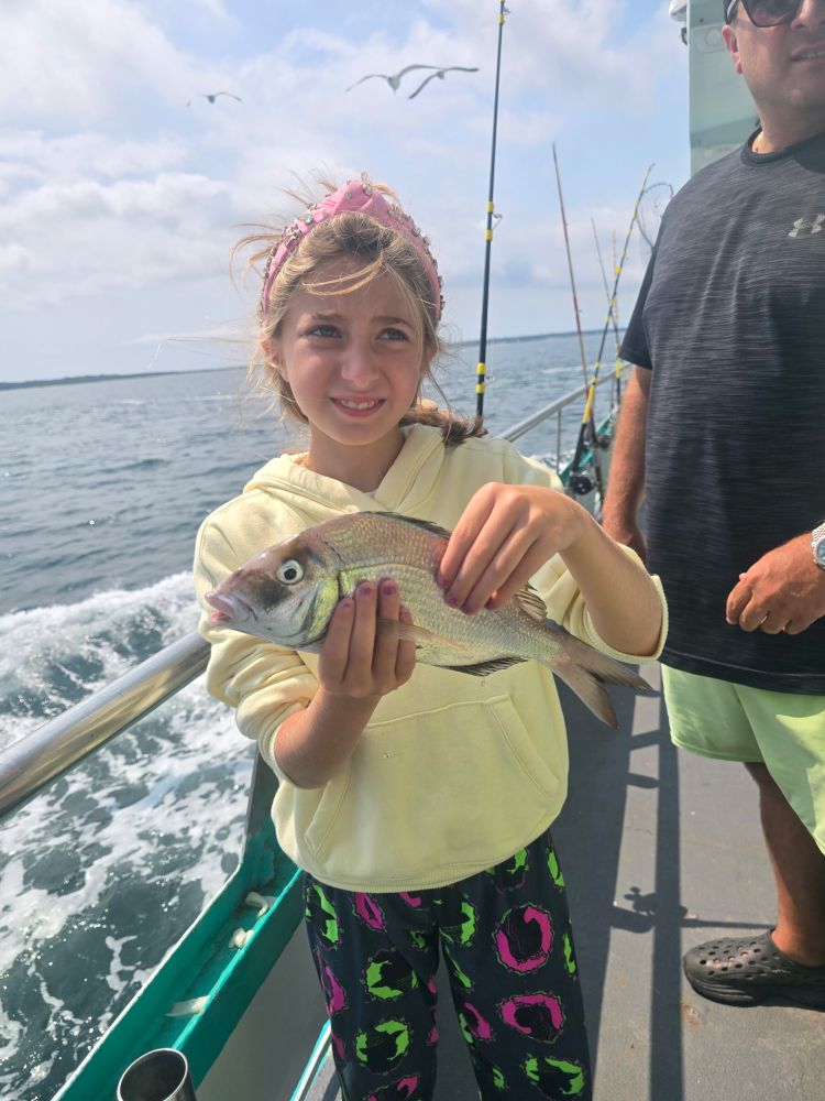 Child on a boat holding a fish, with an adult nearby and fishing rods in the background.