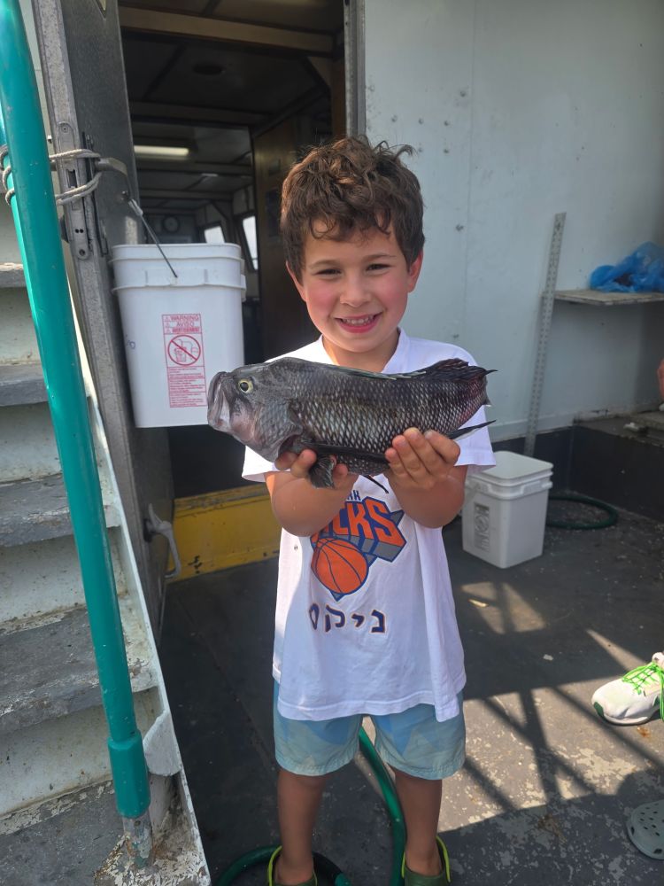Child smiling and holding a fish on a boat deck.