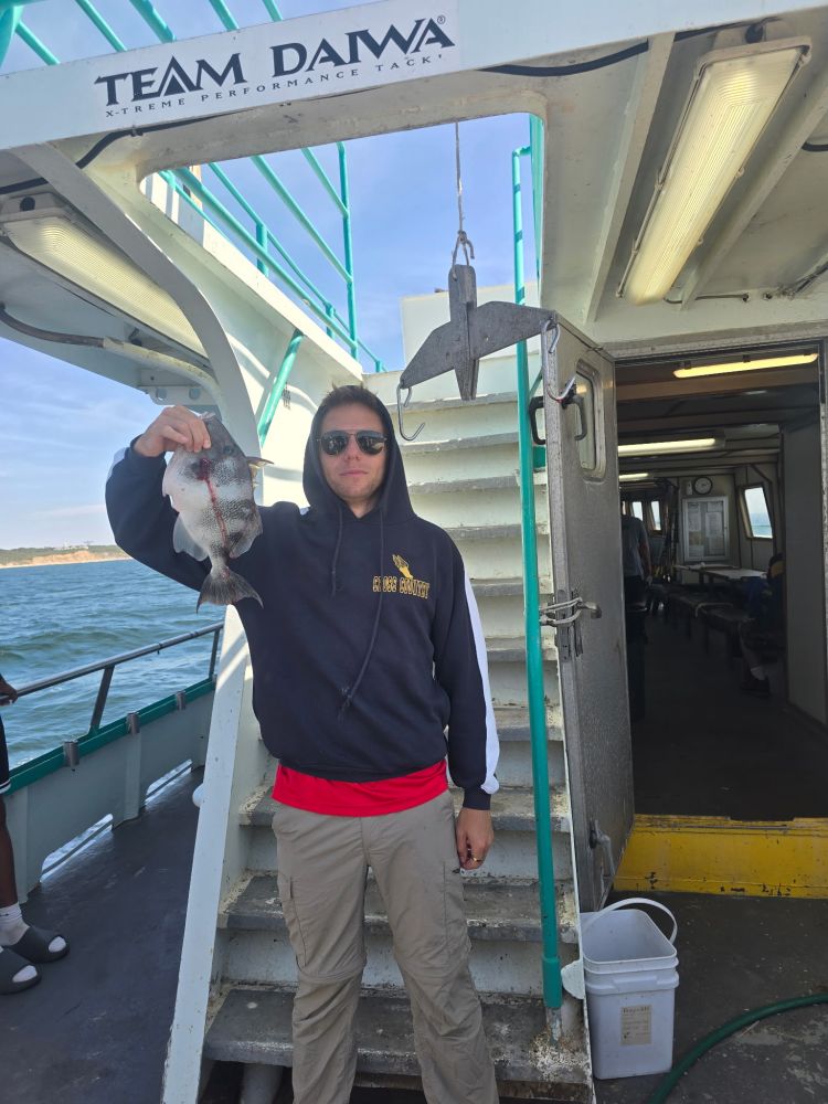 Person holding a fish on a boat with a Team Dawa sign overhead.