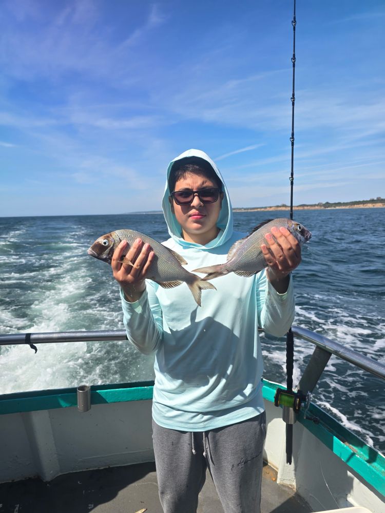 Person on boat holding two fish with ocean in background.