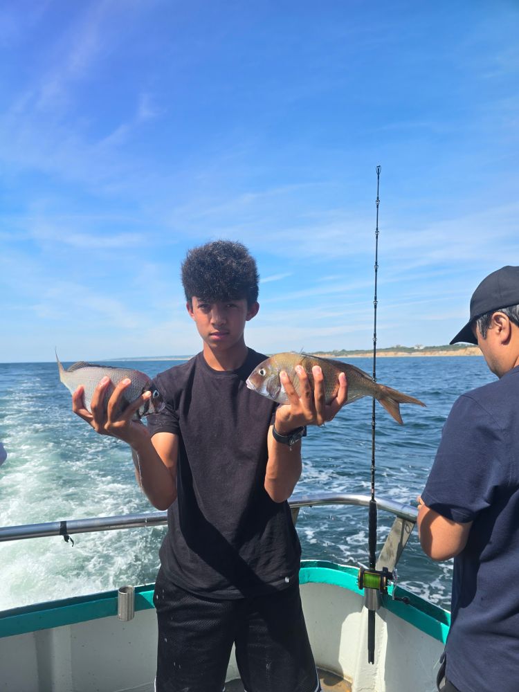 Two people on a boat fishing, one holding two fish.