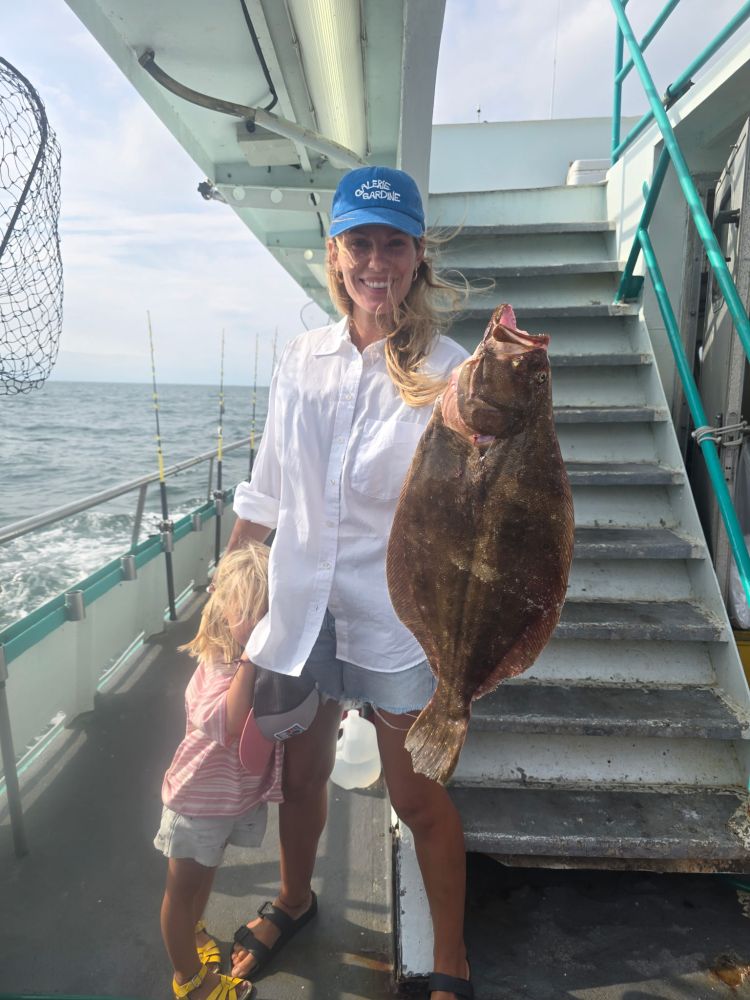 Person on a boat holding a large fish, with a child standing beside them.