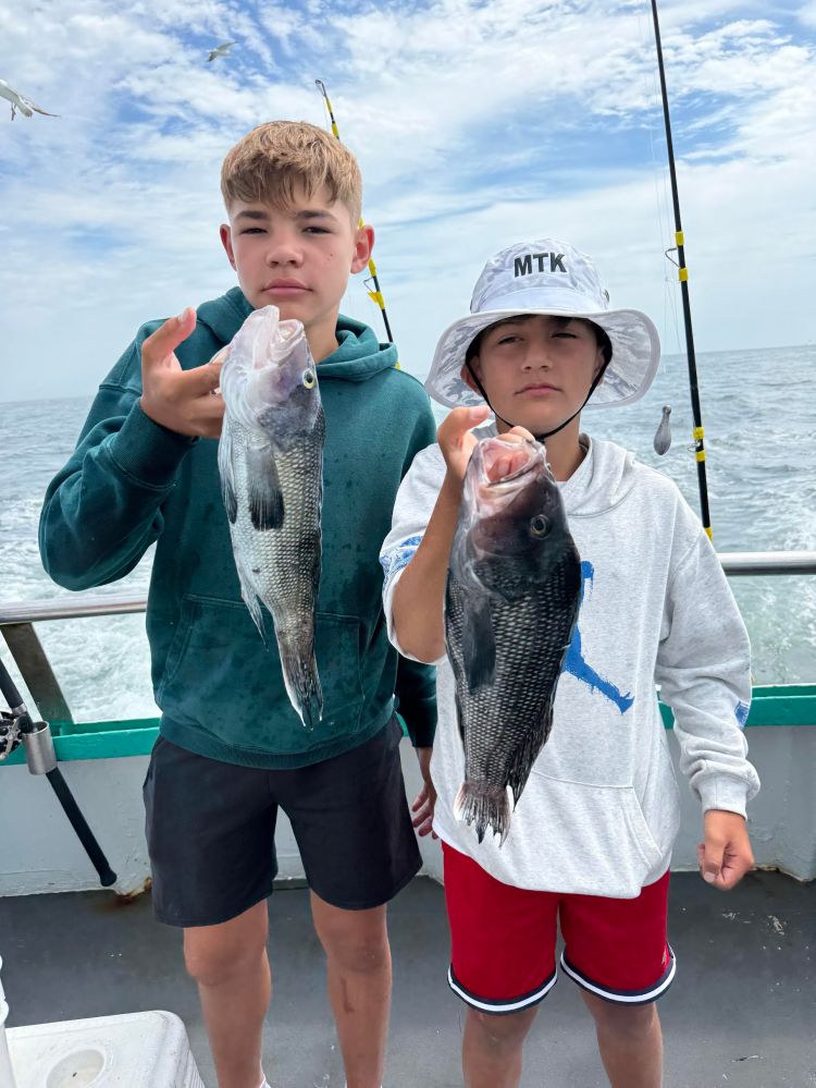Two boys on a boat holding fish, ocean background.