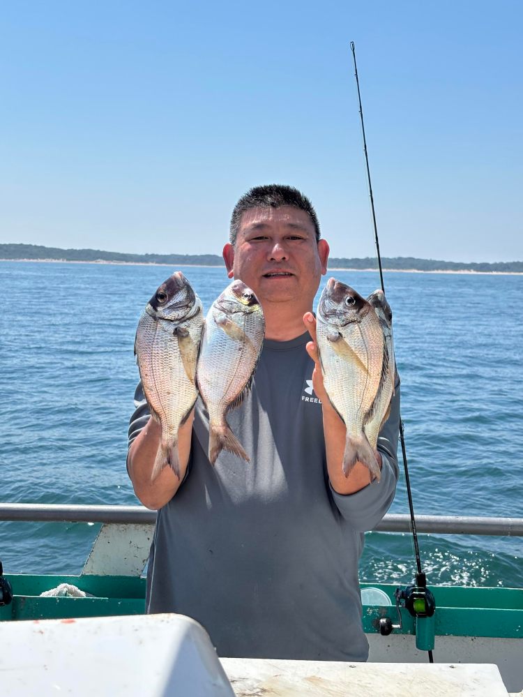 Person on a boat holding four fish with the ocean in the background.