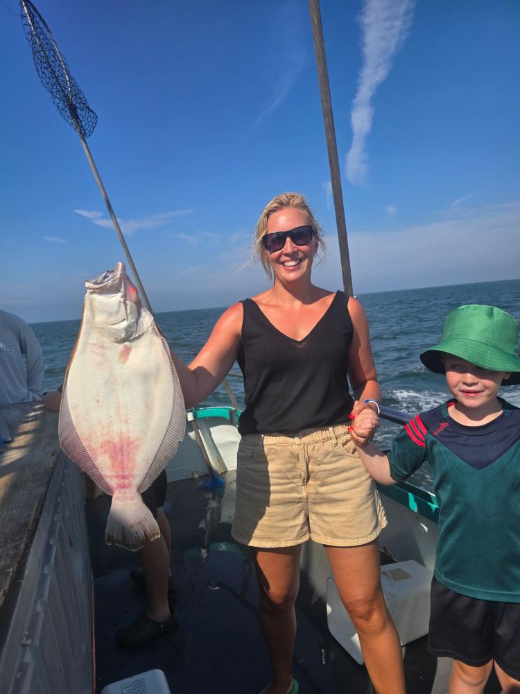 Woman holding a large fish on a boat, standing with a child wearing a green hat.
