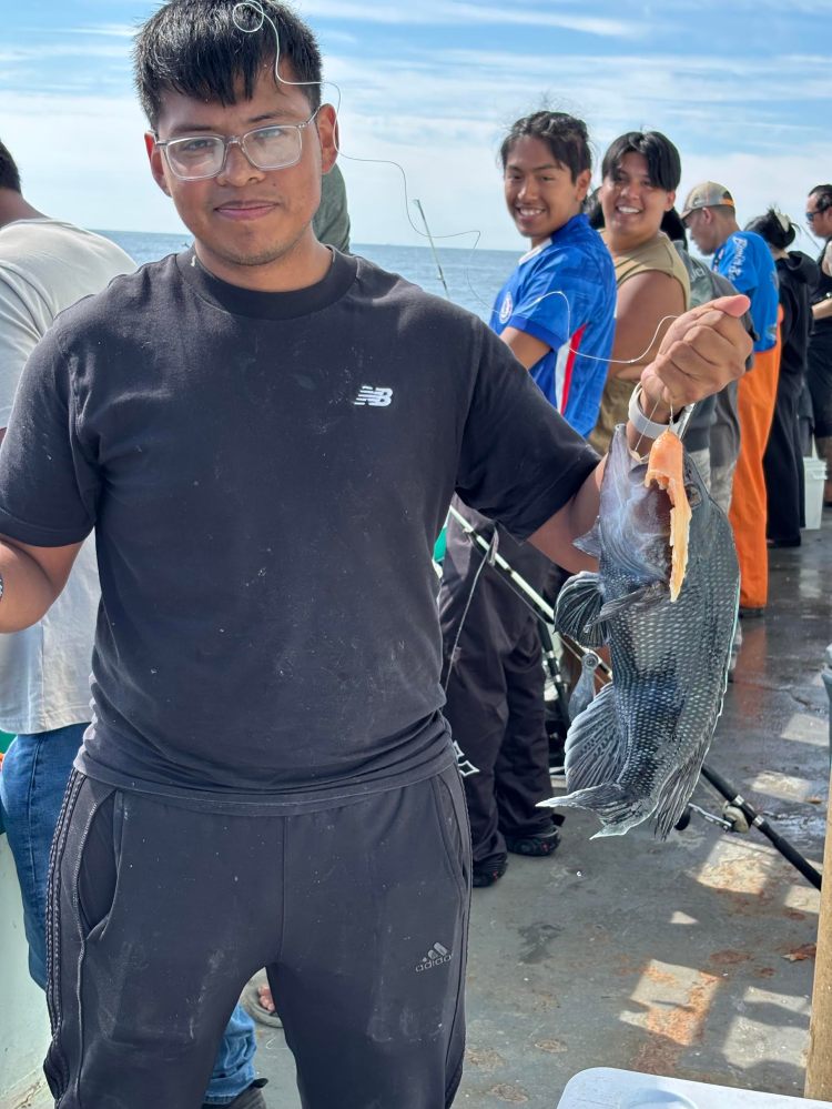 Person holding a large fish on a boat, with others fishing in the background.