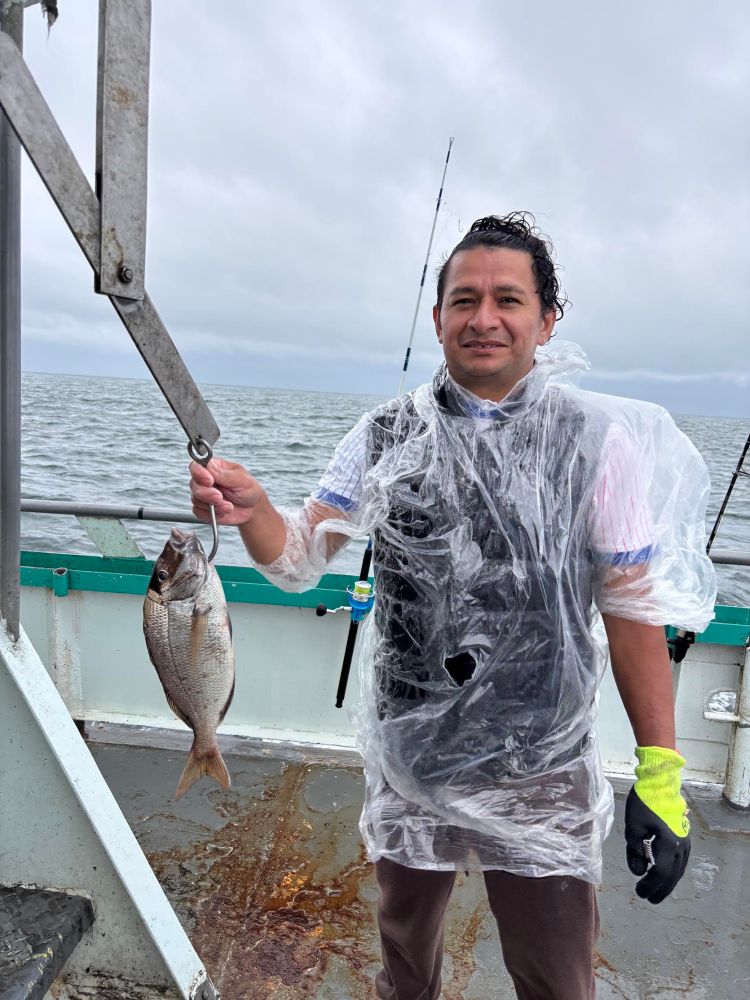 Man wearing a rain poncho holds a fish on a boat with ocean background.