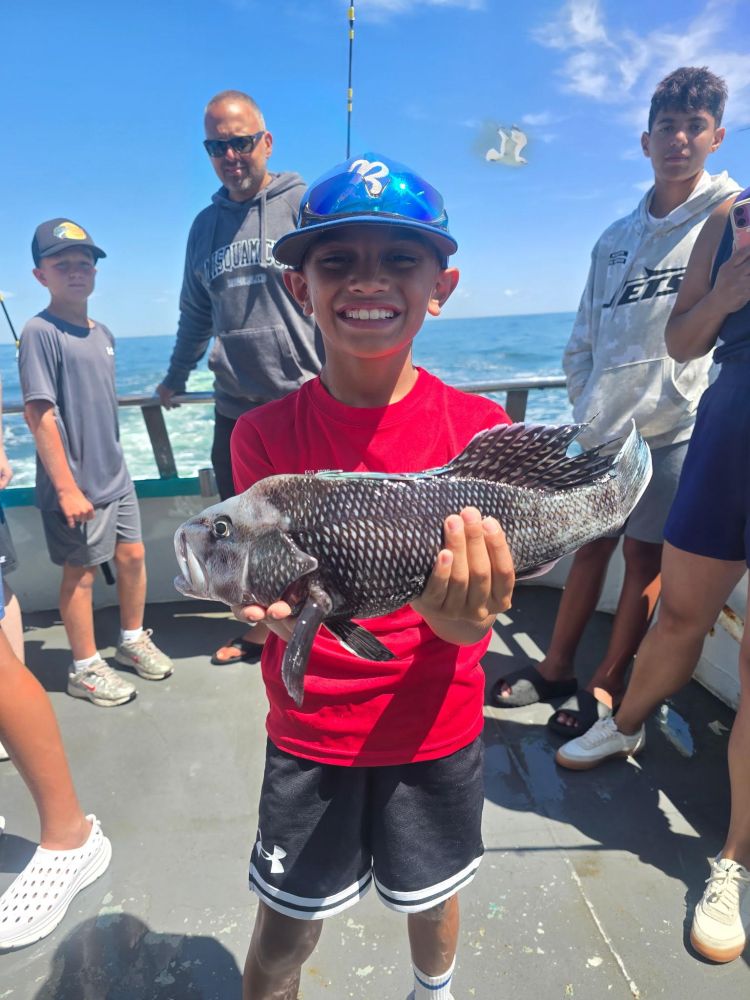 Boy in red shirt holding a fish on a boat; group of people in background.