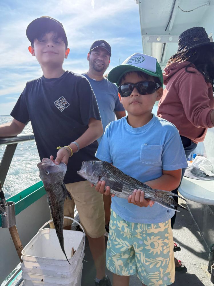 Two children holding fish on a boat, with two adults behind them.
