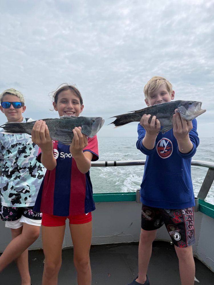Three kids on a boat holding fish under a cloudy sky.