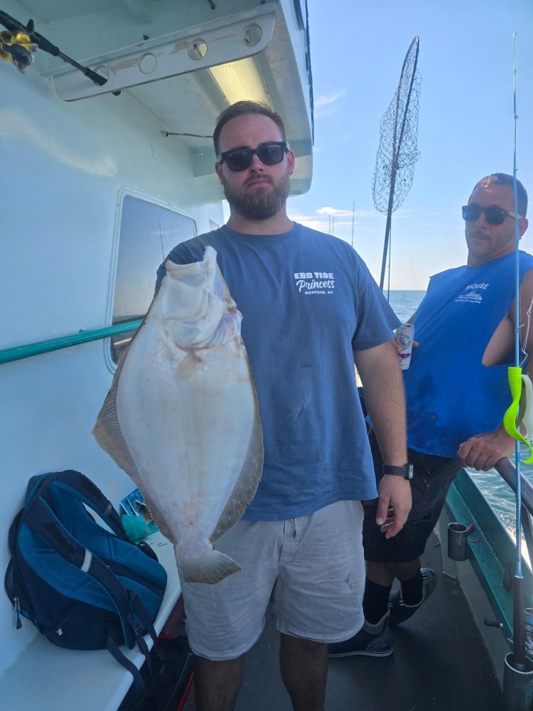 Man on boat holding a large flat fish with another man nearby.
