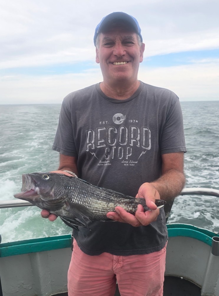 Man smiling on a boat holding a fish against an ocean backdrop.