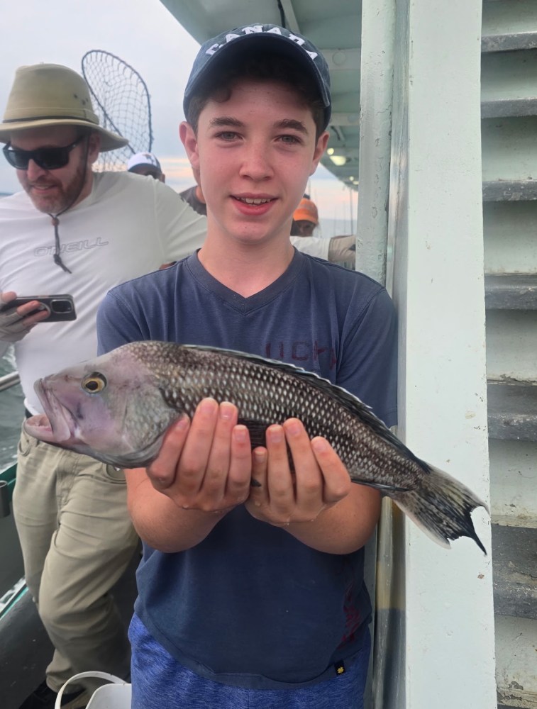Boy holding a fish on a boat with a man in the background.