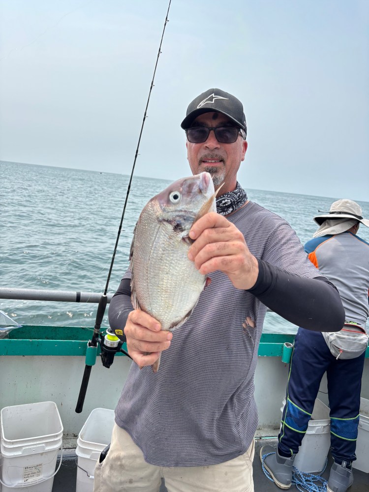 Man on boat holding a fish with ocean background.