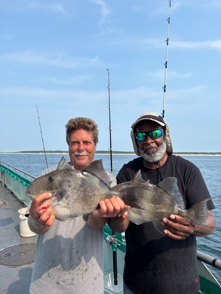 Two men holding fish on a boat under a clear sky.