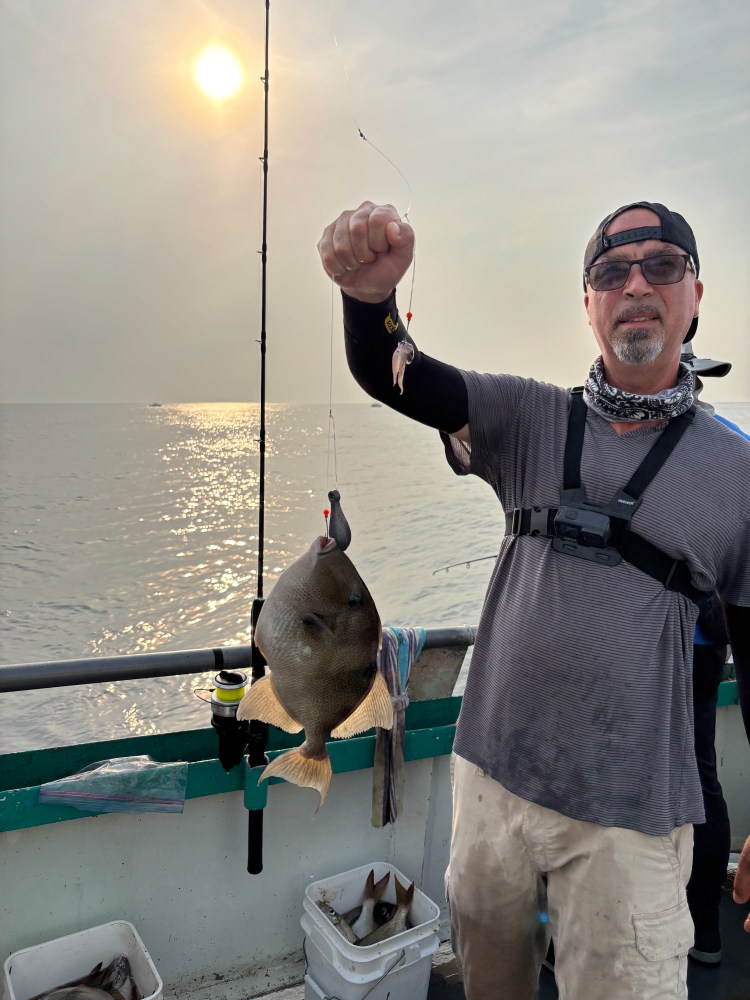 Man holding fish on boat with sunset in background.