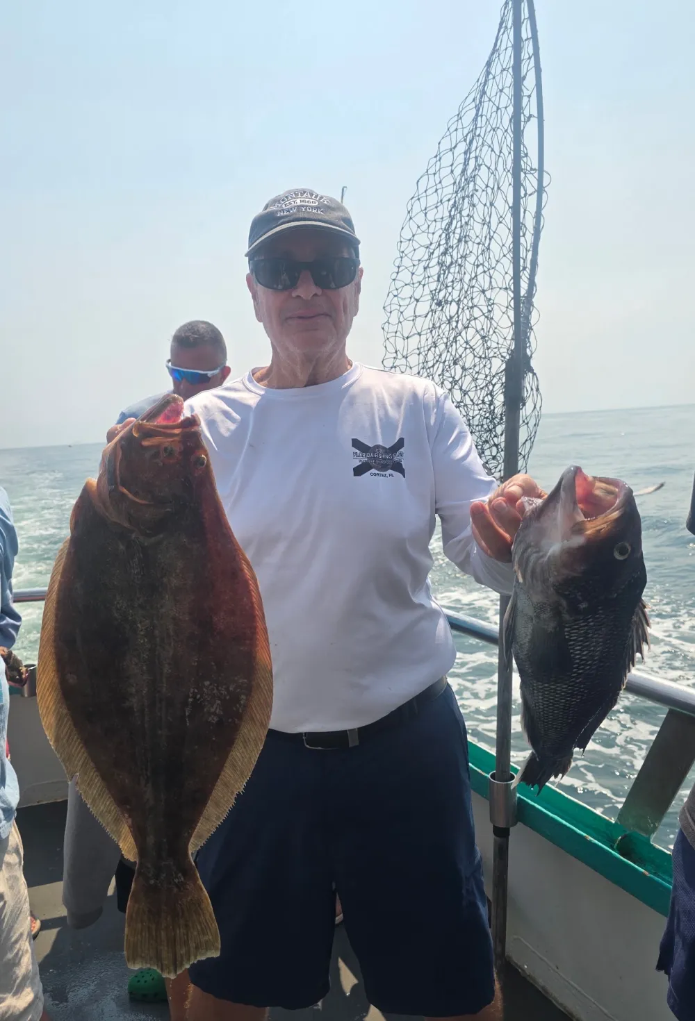 Person holding two large fish on a boat with a net in the background.