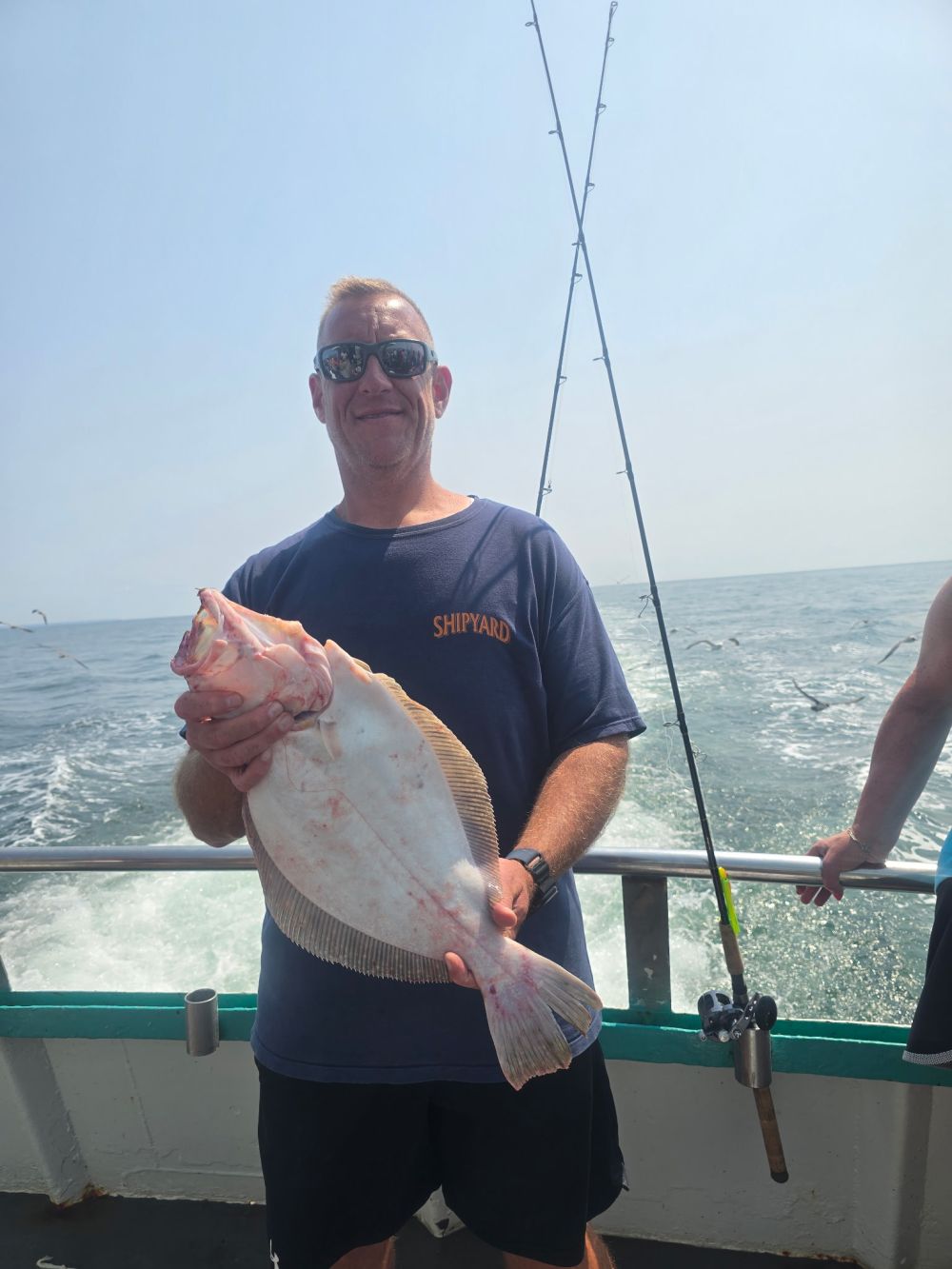 Man holding a large fish on a boat, with ocean in the background.