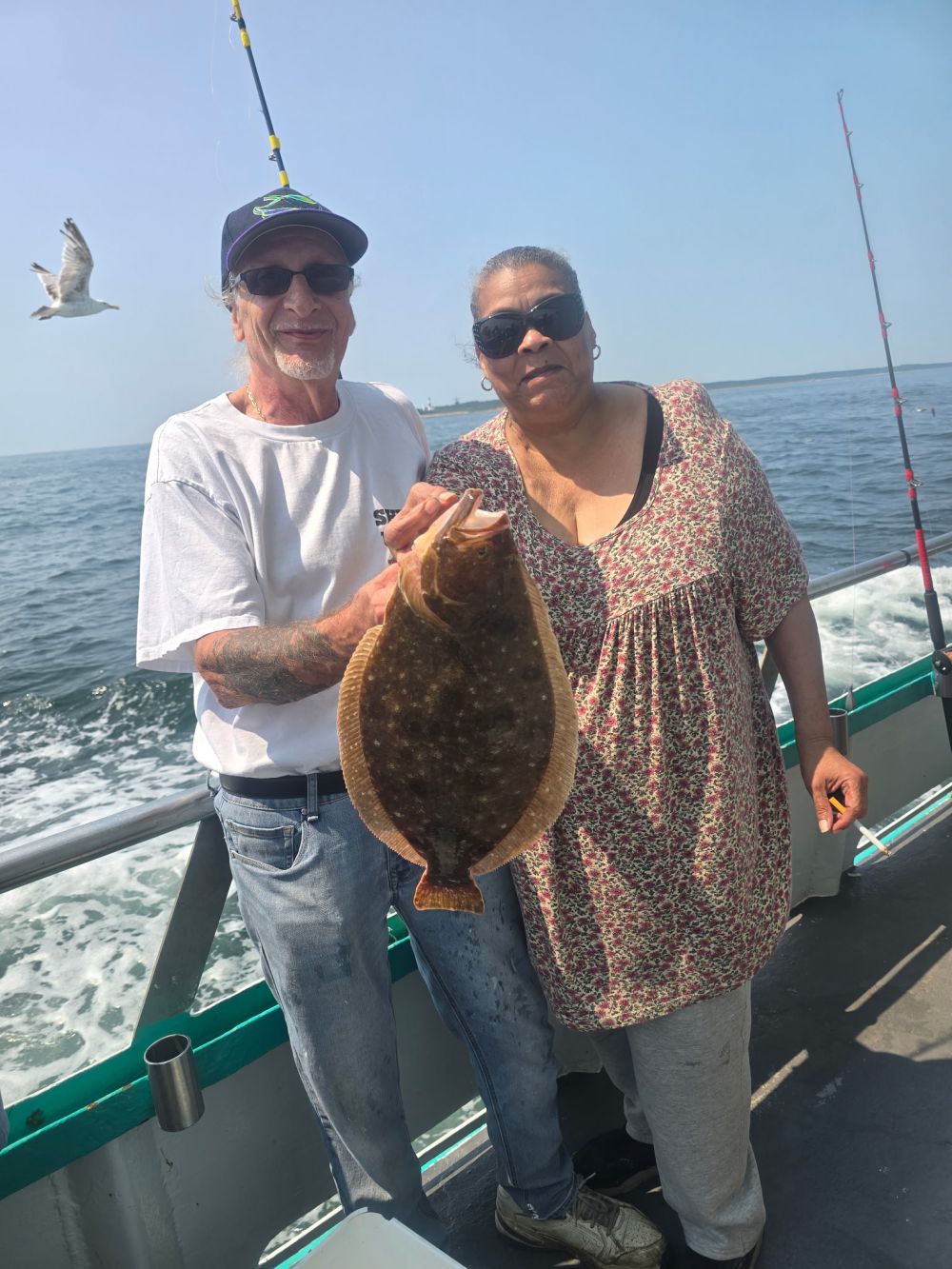 Two people on a boat holding a large fish, with ocean in the background.
