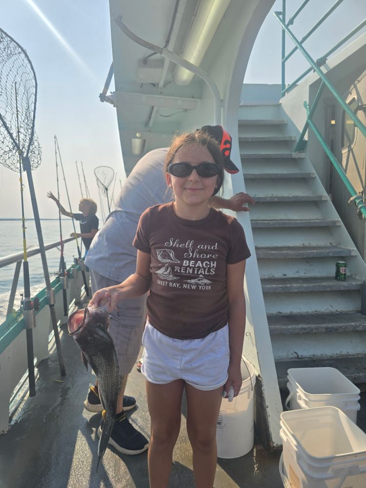 Girl on boat holding fish, wearing sunglasses and a brown t-shirt.