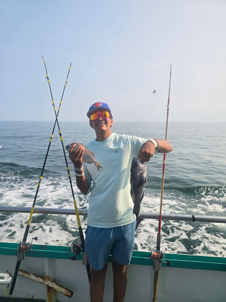 Person on boat holding two fish with ocean in background.