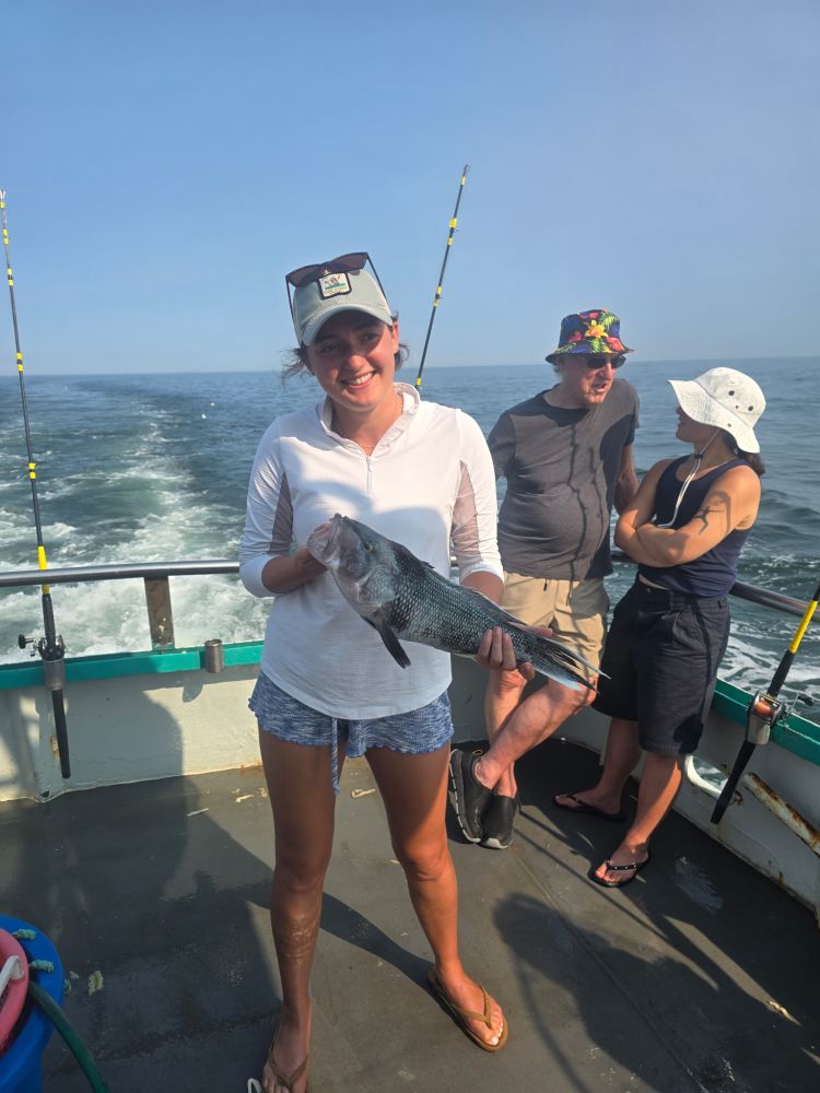 Person holding a fish on a boat deck at sea with two people in the background.