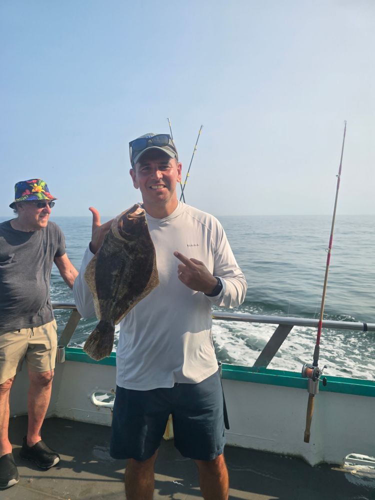 Man holding fish on boat, ocean in background, another person nearby.