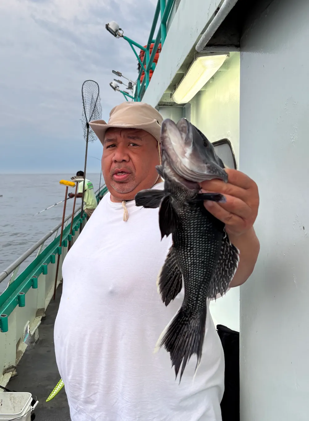 Man on a boat holding a large fish, with ocean in the background.